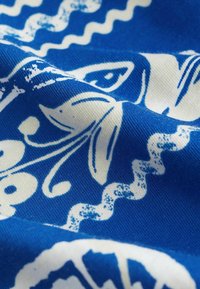 Tissu bleu avec des motifs floraux blancs et des lignes ondulées en vue rapprochée, montrant la texture et les plis du tissu.