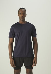 Navy blue short-sleeve athletic shirt with round neckline, soft texture, and minimal logo detail. Worn with black athletic shorts.