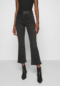 Jeans svasati in denim nero con passanti per cintura decorativi, vita alta e orlo grezzo. Vestibilità casual, accentuata da un tessuto elegante e testurizzato.