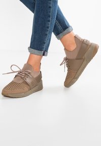 Zapatos deportivos marrones con parte superior perforada, texturas contrastantes y cordones. Cuenta con una suela resistente y soporte acolchado para el tobillo.