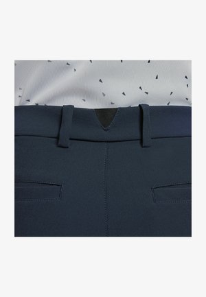 Navy blue bukser har en glat tekstur, bæltestropper og en trekantet detalje bagpå. Forsiden har to dekorative lommer.