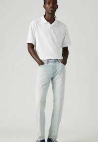 White polo shirt, light blue jeans, and navy sneakers. Polished look with side pockets, subtle contrast stitching on jeans. Smooth fabric texture.