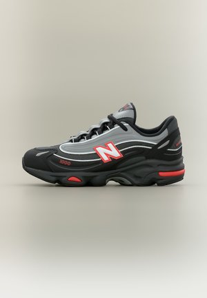 Sort og grå New Balance 1000 sneaker med røde accenter og logo, vist på en ensartet lys grå baggrund.