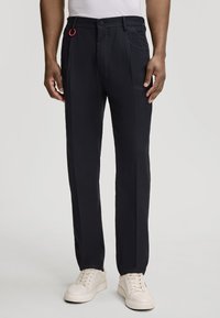 Pantalons navy à coupe droite, dotés d'une fermeture avec bouton visible et d'une boucle rouge en accent. Le matériau semble lisse et léger.