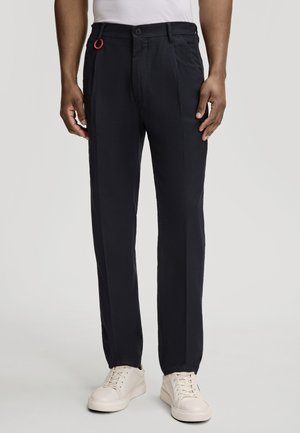 Pantaloni navy con una vestibilità dritta, caratterizzati da una chiusura con bottone visibile e un dettaglio in loop rosso. Il materiale sembra liscio e leggero.