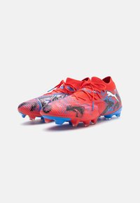 Scarpe da calcio atletiche rosse con superficie testurizzata, accenti blu, lacci e un motivo grafico dinamico con un design nero.