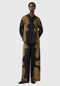 Black satin shirt and wide-leg pants set with gold ornate patterns. Oversized fit, button-down collar, and long sleeves. Flat footwear visible.