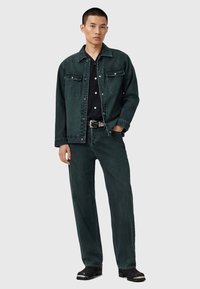 Mørkegrøn denimjakke med to brystlommer, parret med matchende lige mørkegrønne jeans, båret med en sort skjorte og bælte.