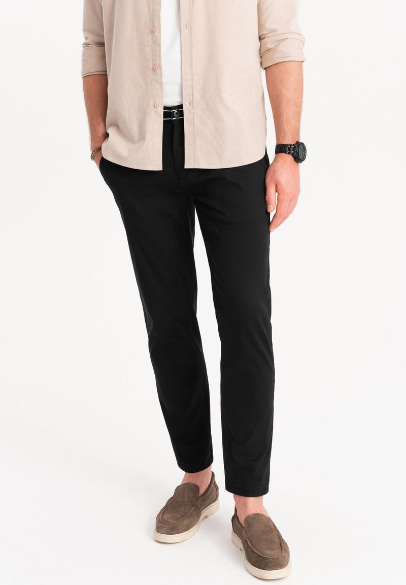 Pantalones negros ajustados de tela de mezcla de algodón, con una textura suave y un diseño de pierna cónica. Combinados con una camisa de botones ligera en color beige.