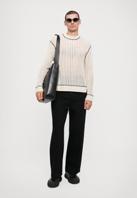 Off-white ribbed sweater with blue stripes, black wide-leg trousers, black vegan leather bag, and sleek black shoes.