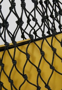 Zwart geknoopt net dat een geel leren ritszakje bedekt tegen een neutrale achtergrond.