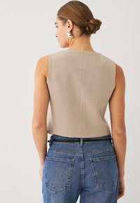 Beige ärmelloses Oberteil mit hohem Ausschnitt und geradem Schnitt, kombiniert mit hochgeschnittenen blauen Jeans aus Denim mit klassischem Fünf-Taschen-Design.