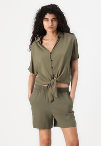 Olive green short-sleeve shirt with a tie knot at the waist, featuring black buttons and matching relaxed-fit shorts with an elastic waistband.