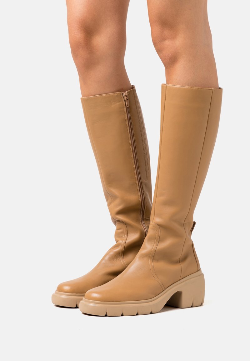 Bottes hautes jusqu'au genou en cuir fauve avec une semelle épaisse beige clair, fermeture éclair latérale et texture lisse, présentant une silhouette ajustée et des coutures minimales.