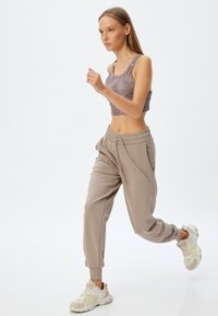 Lys brun crop top med en glat tekstur, parret med løse, beige joggers med elastisk talje og sidelommer. Hvide sneakers.