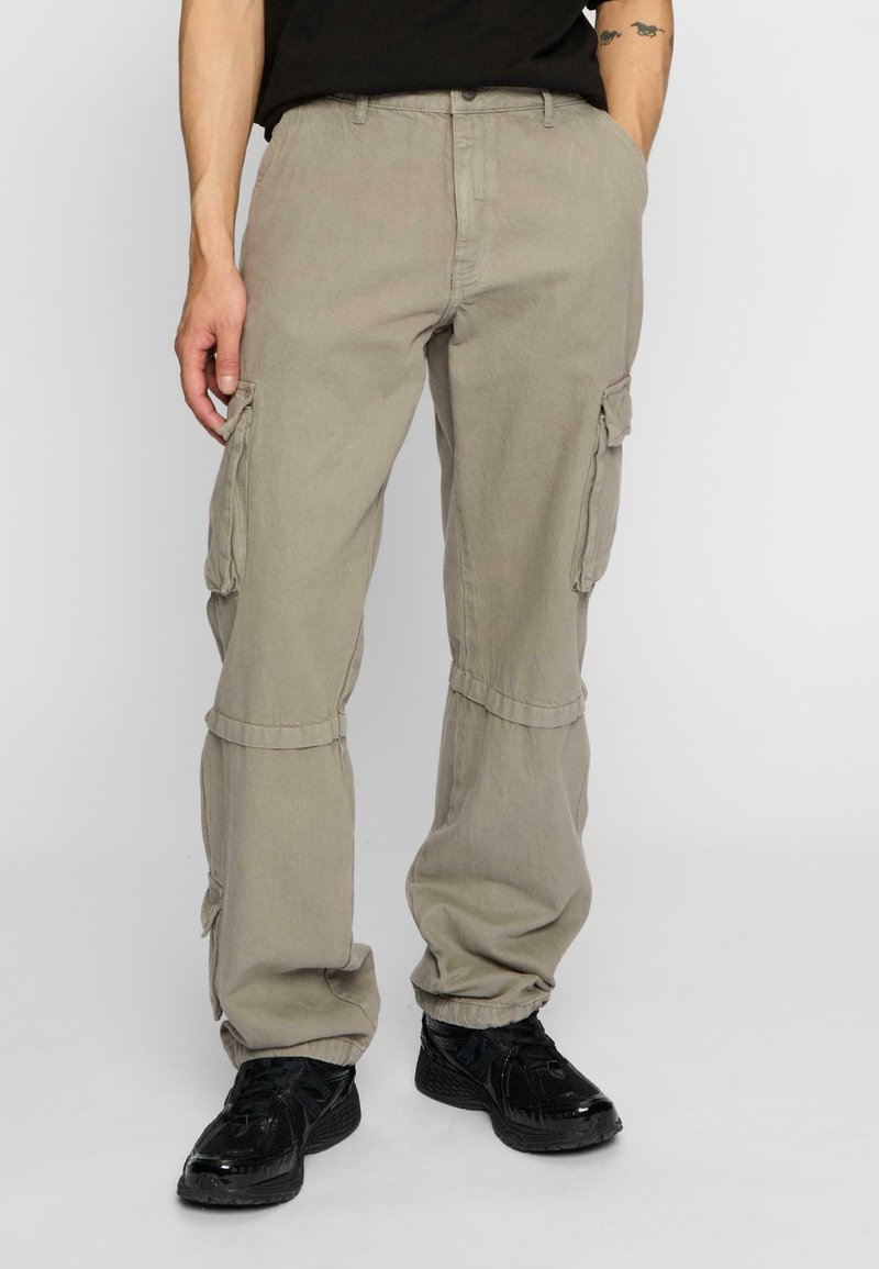 Pantalons cargo beiges avec poches latérales, coupe décontractée et poignets élastiques aux chevilles. Fabriqués en tissu durable avec une texture douce.