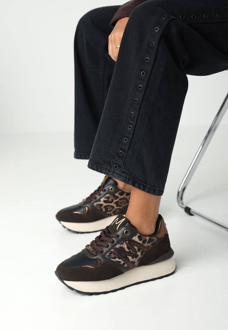 Hnědé a černé tenisky s designem leopardího vzoru a semišovými detaily. Mají gumovou podrážku a kontrastní textury.