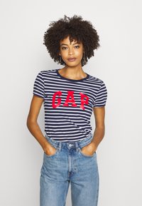 Navy and white striped t-shirt featuring red "GAP" logo, round neck, and short sleeves, paired with high-waisted light blue jeans.