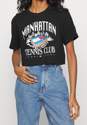 Czarny krótki t-shirt z kolorową grafiką kortu tenisowego w Manhattanie i tekstem, zestawiony z niebieskimi, wysokim stanem dżinsami na osobie.