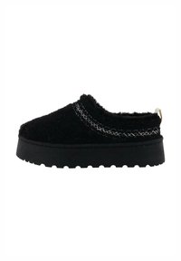 Czarne buty wsuwane wykonane z teksturowanej tkaniny z grubą czarną podeszwą i metalicznymi przeszyciami wzdłuż górnej krawędzi.