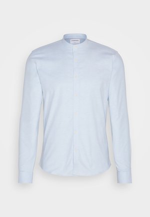 Camisa de manga longa azul-claro com colarinho mandarim, apresentando um fecho de botões e um tecido suave e texturizado. Corte ajustado com barra arredondada.