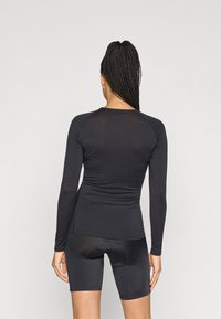 Musta pitkähihainen slim fit -paita, jonka pinta on sileä ja onde raglan-hihat, yhdistettynä mustiin pyöräilyshortseihin, joissa on pehmustettu istuinalue.