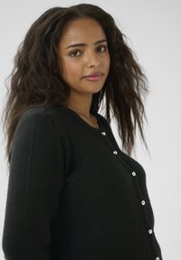 Schwarze Strickjacke mit Rundhalsausschnitt und silbernen Knöpfen vorne. Der Stoff hat eine weiche Textur und einen lockeren Schnitt.
