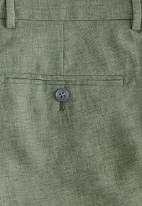 Tissu vert olive à finition texturée, doté d'une poche à rabat et d'une fermeture par bouton foncé à quatre trous.