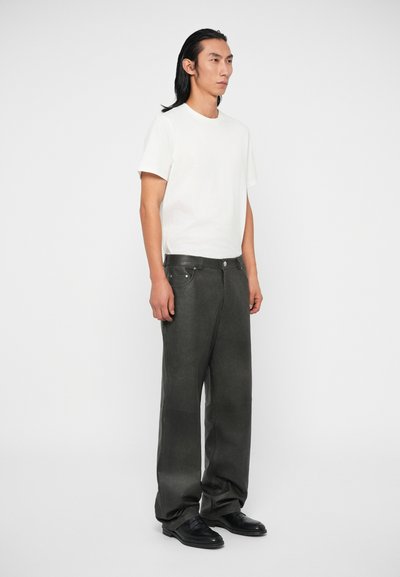 Camiseta blanca de manga corta combinada con pantalones anchos gris oscuro. Los pantalones presentan una textura suave y bolsillos frontales tradicionales. Zapatos negros.