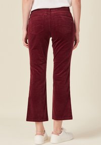 Bordeaux corduroy flared broek met achterzakken met kromme naden en een zachte textuur, gecombineerd met witte sneakers.