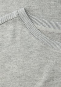 Tissu de t-shirt gris clair avec une finition texturée et douce ; comporte un col rond côtelé et des coutures nettes. Aucun motif ou graphique visible.