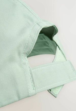 Svjetlozelena odjeća s teksturiranim materijalom, dijagonalnim šavovima i podesivim remenom s kvadratnim izrezom.