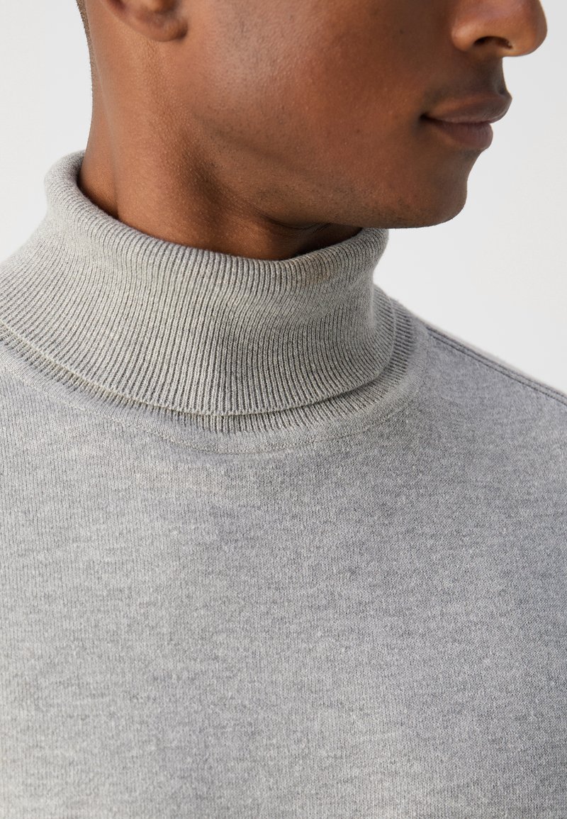 Pull col roulé gris avec un col côtelé, présentant une texture lisse et une coupe près du corps, montré de profil.