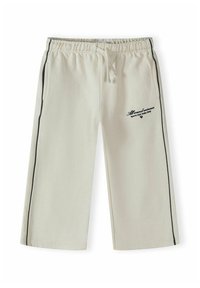 Pantalon de survêtement large couleur blanc cassé avec bandes latérales noires, taille élastique avec cordon de serrage, et texte à l'avant droit "All around winners Sports Club Italia 1993."