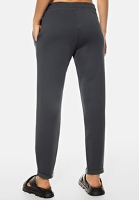 Donkergrijze taps toelopende joggers gemaakt van zachte stof met een elastische tailleband, zijzakken en opgerolde manchetten, gecombineerd met zwarte sandalen.