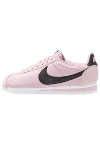 Rosa träningsskor med en svart Nike-swoosh. Har en slät syntetisk ovandel, rund tå, snörningsdesign och texturerad gummisula.