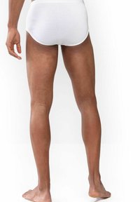 Weiße Baumwollslips mit glatter Textur, hoch geschnitten und in runder Form, von hinten mit nackten Beinen und Füßen gezeigt.