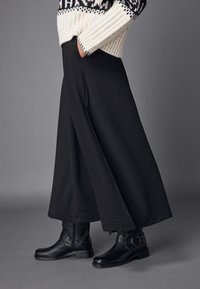 Jupe noire texturée au design fluide. Associée à des bottines noires à bride latérale et à talon épais. Le pull présente un empiècement à motifs.