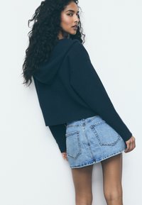 Felpa corta blu navy con cappuccio, abbinata a una minigonna in denim azzurro chiaro con tasche posteriori e orlo sfilacciato.