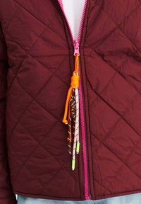 Burgundský prošívaný kabát s růžovým zipem a barevnými akcenty na tkaničkách. Látka má mírně lesklou strukturu s diamantovými vzory.