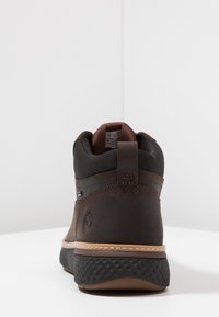 Bruine leren enkelboot met een gestructureerde rubberen zool, een glad bovenwerk en een gevoerde kraag; heeft een gestikte naad en merklogo aan de zijkant.