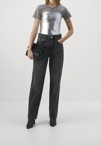 Silverfärgad topp med grå korta ärmar, kombinerad med hög midja svarta jeans och en svart handväska. Svarta spetsiga ankelskornor fulländar looken.