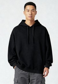 Sudadera con capucha negra de corte relajado con un bolsillo canguro, capucha con cordón y puños acanalados. Confeccionada con tela suave, diseño minimalista.