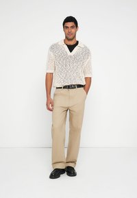 Krémový krátký svetr s otevřeným vzorem, spárovaný s béžovými kalhotami. Kompletu doplňuje černý pásek a černé boty.