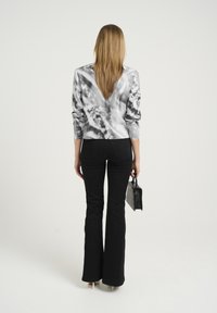 Pantaloni neri a campana abbinati a una blusa grigia tie-dye. La blusa presenta un design corto e maniche lunghe, con una texture liscia.