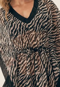 Kaftan w wzór zebry z czarnym dekoltem w serek, ściągniętą talią z marszczonym materiałem oraz przezroczystym, teksturowanym materiałem. Czarny wykończenie wzdłuż krawędzi.