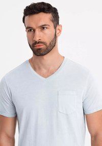 Světle modré tričko s výstřihem do V vyrobené z měkké tkaniny, s krátkými ohrnutými rukávy a kapsou na hrudi, s hladkým a minimalistickým designem.