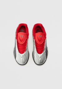 Sneakers argento con lacci e dettagli rossi, caratterizzati da un design testurizzato e una suola nera. Logo PUMA sulla linguetta e sul lato.