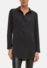 Schwarzes Langarmshirt aus glattem Stoff, mit Kragen, Knopfleiste und abgerundetem Saum, kombiniert mit schmalen schwarzen Hosen.