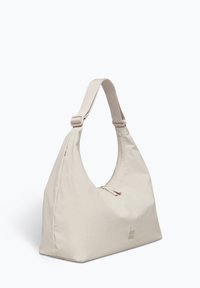 Beige Stofftasche mit asymmetrischem Design, rundem Henkel und Reißverschluss an der Oberseite. Auf einer Seite befindet sich ein prägendes Logo. Glatte Textur.